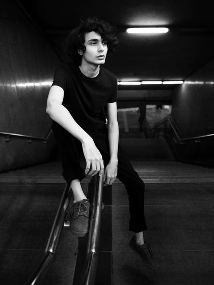 A young man on a staircase railing in an underpass. The dark, moody environment and his contemplative pose give this black and white photo a cinematic feel.