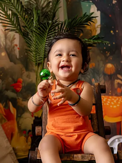 A big, happy laugh during a jungle-themed photoshoot. The setup includes a friendly stuffed monkey, a teepee tent, and a vibrant forest backdrop for a fun safari adventure.