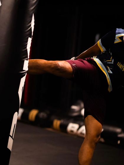 A fighter throws a powerful kick at a heavy bag, demonstrating the force generated in Muay Thai.