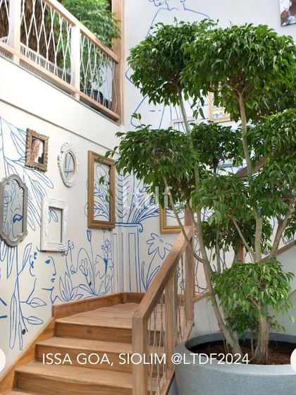 The staircase at ISSA Goa is a canvas for local art, with whimsical line drawings and curated frames creating a gallery-like experience. A large potted tree brings nature indoors, reinforcing the connection between the design and its lush surroundings.