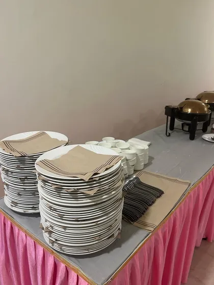 A neat stack of plates and cutlery on a buffet table with a pink skirt. I take care of all the details.