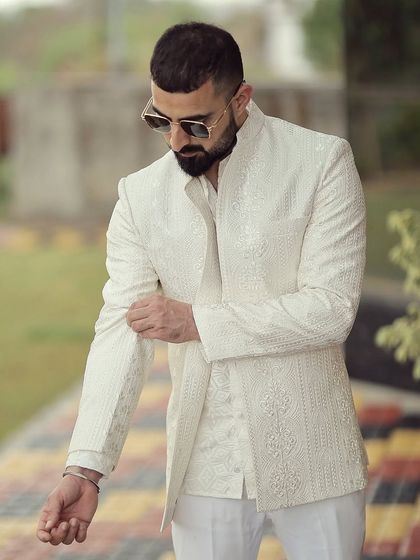 Every detail matters in a bespoke creation. Our client adjusts his sleeve, showing the perfect fit and texture of his custom-made ivory Bandhgala jacket, designed for his special day.