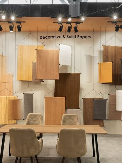 A visitor examines the suspended wood panel samples at the Ambica stall. This interactive display method allows for close inspection of the products and adds to the industrial yet elegant aesthetic of the space.