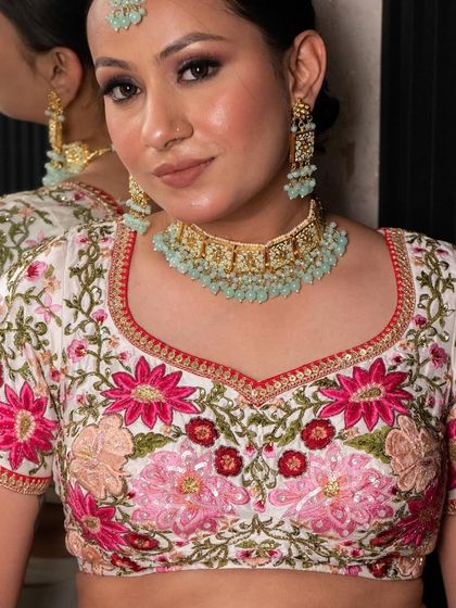 This white lehenga with vibrant pink and red floral embroidery is a fresh and beautiful look for a day wedding or sangeet. The blouse is intricately detailed for a stunning effect.