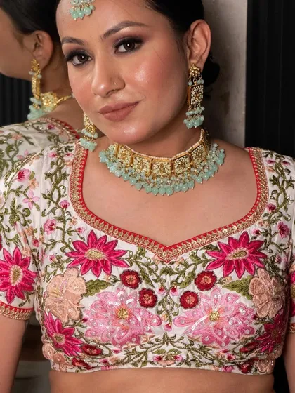 This white lehenga with vibrant pink and red floral embroidery is a fresh and beautiful look for a day wedding or sangeet. The blouse is intricately detailed for a stunning effect.