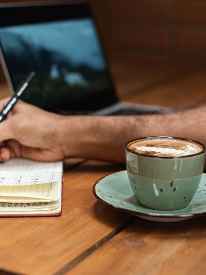 The perfect setup for a productive morning: a notebook, a pen, a laptop, and a fresh cup of our specialty coffee.