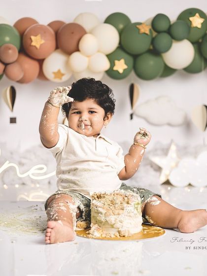 A full-body shot of a one-year-old enjoying his cake smash. The hot air balloon theme in earthy tones is modern and sweet.