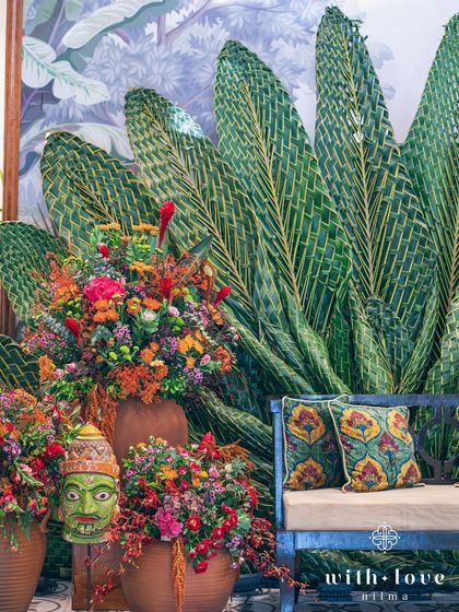 A detail of the Pellikuthuru ceremony decor, with a traditional mask and vibrant flowers set against the woven leaf backdrop.