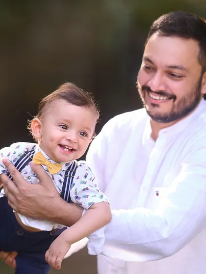 A happy father holding his smiling baby, who is dressed smartly in a bow tie and suspenders. This image showcases a mix of playful energy and sweet style.