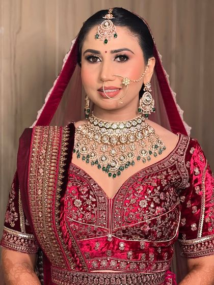 A classic bridal portrait. This bride is wearing a beautiful red velvet lehenga with green jewellery, and her makeup is soft yet defined.