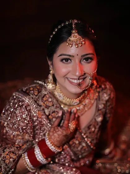 A happy, welcoming portrait of a bride in a maroon lehenga, her hands in a gesture of namaste.