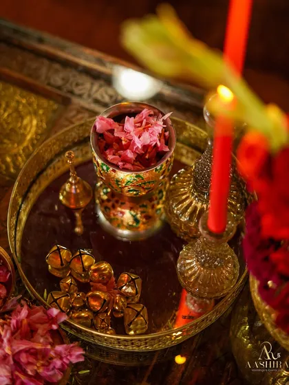 A detail shot of a mirrored tray holding a decorative glass filled with petals, golden bells, and red taper candles, embodying the event's rich aesthetic.