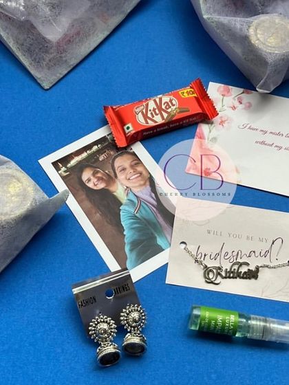 Our budget-friendly bridesmaid hampers are packed with love. Each organza bag contains a personalised polaroid, a candle, earrings, perfume, and a KitKat, making it a perfect token of appreciation.