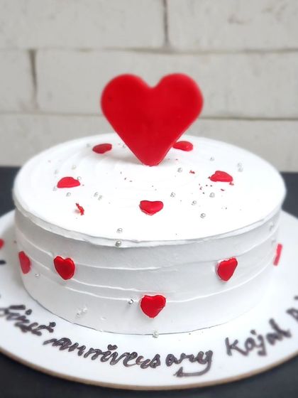 A classic white anniversary cake decorated with a cascade of red hearts. This design is perfect for celebrating a first anniversary or any romantic milestone.