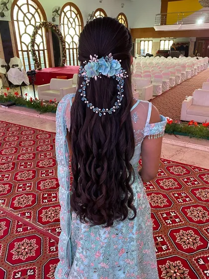 A stunning reception hairstyle with long, flowing waves and a beautiful blue floral hair accessory that matches the bride's lehenga.