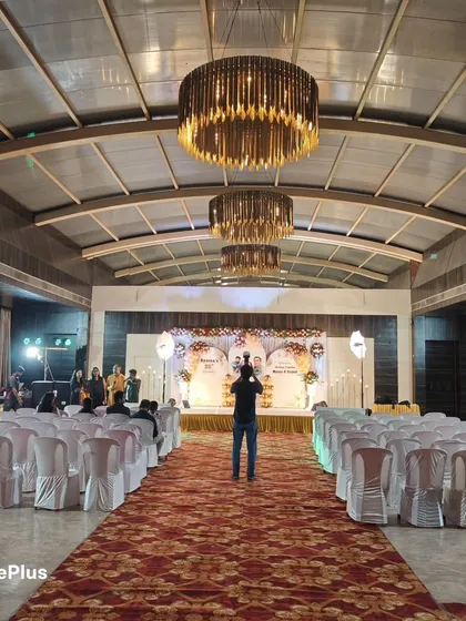 A wide shot of a banquet hall set up for a 25th birthday or anniversary celebration. I handle the stage decor, seating arrangements, and the overall lighting to create a grand and festive atmosphere.