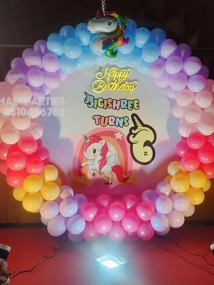 A circular balloon backdrop with a rainbow unicorn theme for a 6th birthday party.