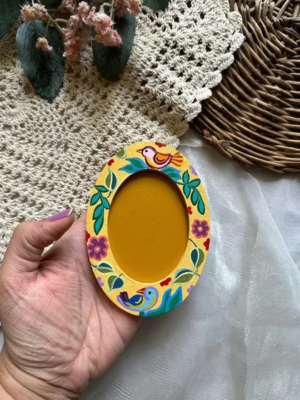 An oval-shaped photo frame magnet with a cheerful bird and floral pattern on a yellow background.