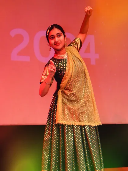A solo performer strikes a confident pose during her classical dance segment at Pehal 2024. The stage lighting and traditional green and gold costume create a memorable moment.