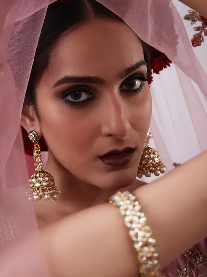 A close-up of a dramatic bridal look with a dark, smokey eye, a deep lip color, and traditional jhumka earrings.