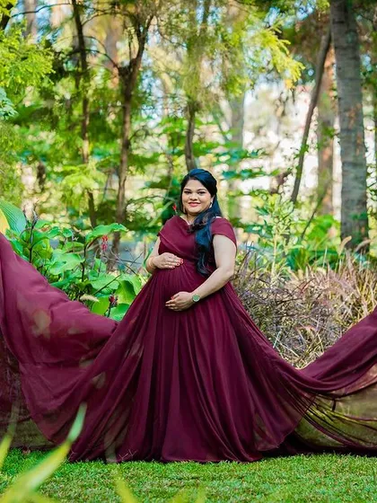 A cinematic solo maternity portrait in a lush garden setting, featuring a dramatic, flowing maroon gown that adds a touch of fairy-tale magic. This style is perfect for creating truly standout images.
