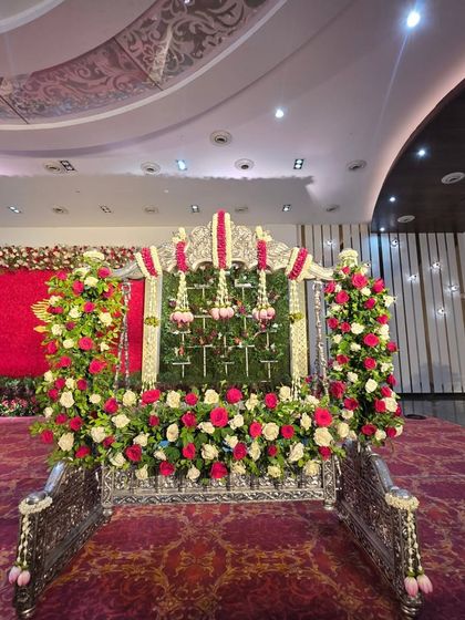 A beautifully decorated silver cradle, adorned with arches of red and white roses, ready for a naming ceremony.