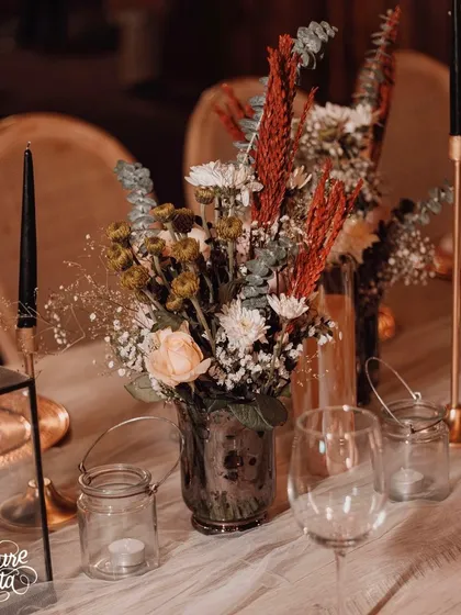 A close-up of a floral centerpiece from the vintage romance theme, featuring a mix of textures with dried and fresh flowers in muted tones, complemented by tall, elegant candles.