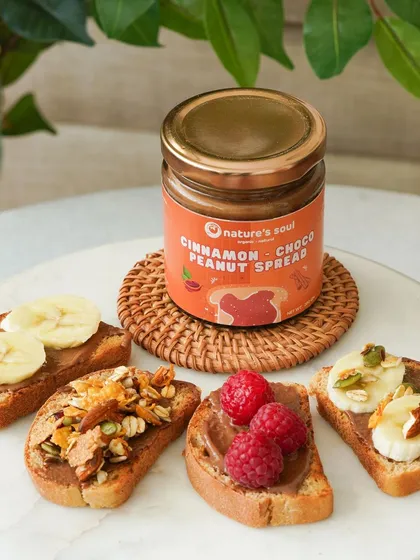 Showcasing the versatility of a cinnamon choco peanut spread with various toppings like banana, raspberries, and granola on toast.