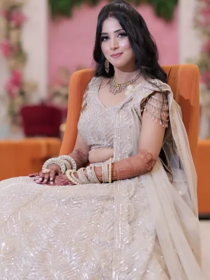 A full-length shot of the bride seated, looking radiant in her golden engagement lehenga.
