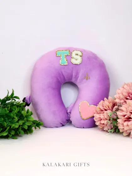 A personalized purple velvet neck pillow with glittery "TS" initials and a heart patch. Travel in comfort and style.