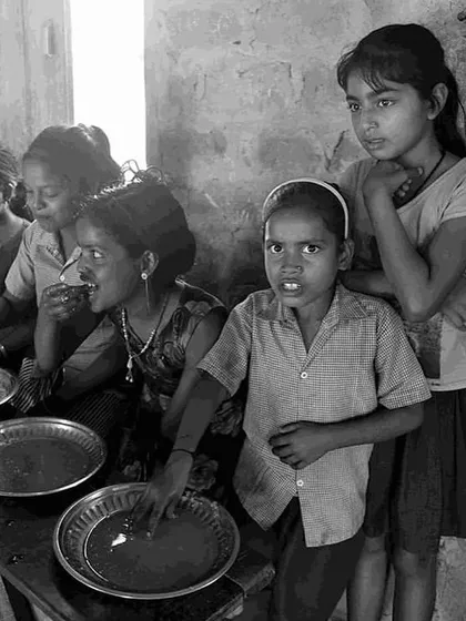 Children and women share a meal at a community centre. This scene from the exhibition illustrates the importance of communal support and nutrition programs in combating hunger.