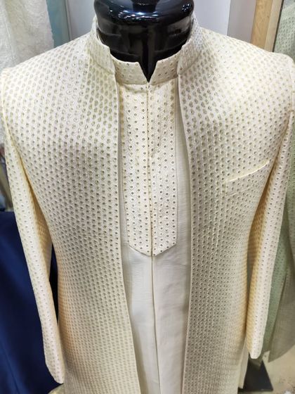 A classic open sherwani jacket in a textured cream fabric, layered over a matching kurta. This is a versatile and elegant choice for any groom.