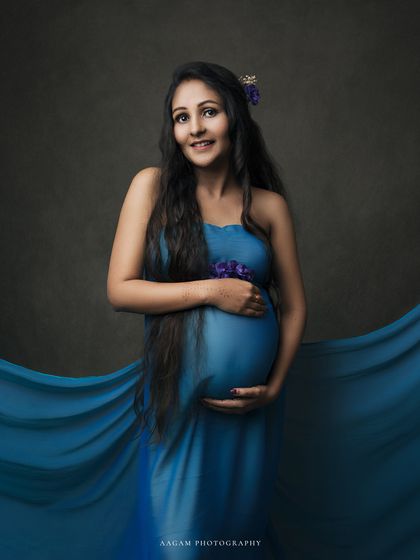 A flowing blue silk drape creates a dreamy, ethereal effect, wrapping the mother-to-be in a wave of color.