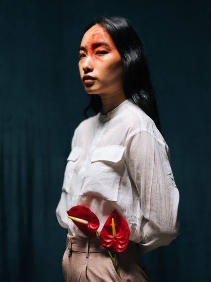 Another portrait from the Label Rama shoot, this time with the flowers held at the waist. The image is moody and atmospheric, with a focus on the contrast between the red flowers and the dark background.
