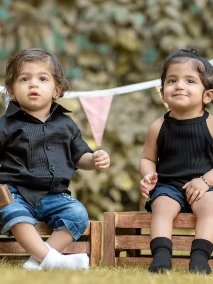 The twin duo, Avyaan and Aanshi, sitting on rustic wooden crates. This portrait showcases their bond, with a festive bunting in the background adding a touch of celebration to the outdoor setting.