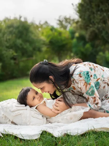 A mother leans over her baby, who is lying on a blanket in the grass. This tender moment is a beautiful example of a lifestyle family photoshoot.