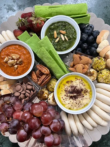 A vibrant grazing board perfect for intimate gatherings. It features a trio of my signature dips: classic hummus, spicy muhammara, and fresh pesto, served with a variety of crackers, breads, fruits, and nuts.
