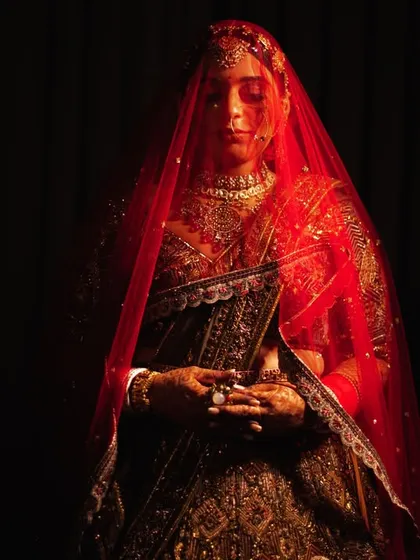 A full-length portrait of the bride under her red veil, shrouded in shadow. A very dramatic and artistic bridal shot.