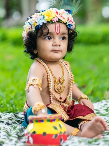 A seated portrait of a baby boy in his Krishna attire, looking thoughtfully to the side.