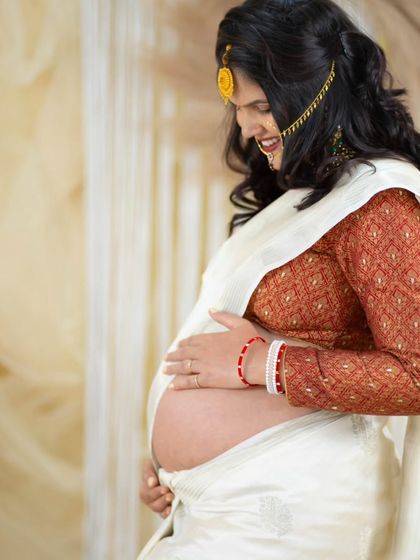 A beautiful close-up of a mom-to-be in a traditional white saree. This shot focuses on her happy expression and the gentle way she holds her baby bump.