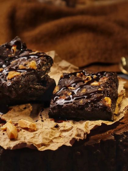 Nothing smells like home more than baking. These rich, fudgy brownies are stacked on a wooden board against a warm, textured background, creating a comforting and delicious scene.