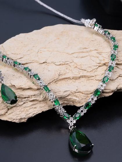 A beautiful emerald and diamond necklace set, elegantly displayed on a piece of natural stone. This styling choice adds an earthy and organic feel to the luxurious jewellery.