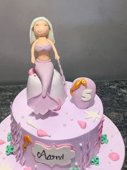 An enchanting mermaid-themed cake in a lovely shade of lavender. It's decorated with a handcrafted mermaid figure, seashells, and a seahorse for an under-the-sea adventure.