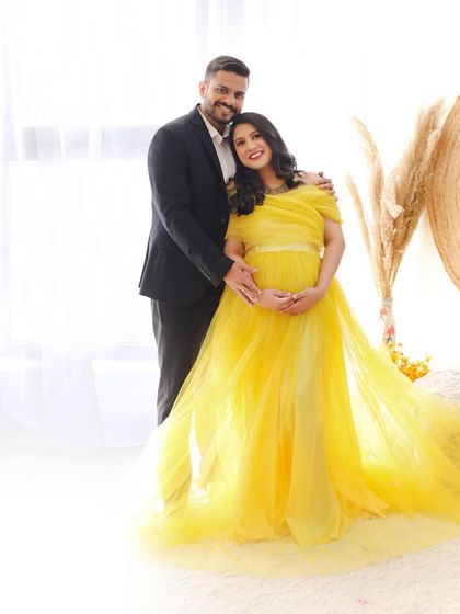 A happy and bright couple portrait. The mom-to-be glows in a yellow tulle gown, perfectly complementing the sunny and cheerful boho studio setup.