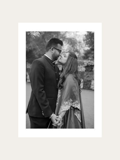 A beautiful black and white portrait of a groom kissing his bride's cheek, a simple and sweet gesture of love.