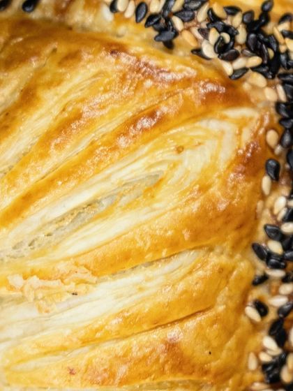 A close-up of the golden, flaky layers of a freshly baked puff pastry, topped with sesame seeds.