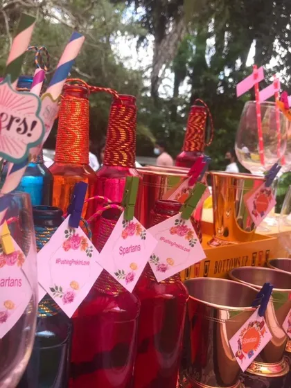 A burst of color and fun for your guests. This image shows a collection of colorful pre-mixed drinks and custom-tagged glasses, ready to be served at a lively outdoor Mehendi or Haldi ceremony.