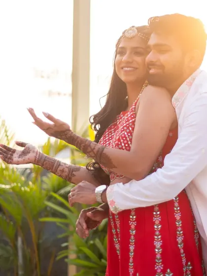 The bride showing off her beautiful mehendi design, wrapped in the groom's arms. A classic and romantic shot.