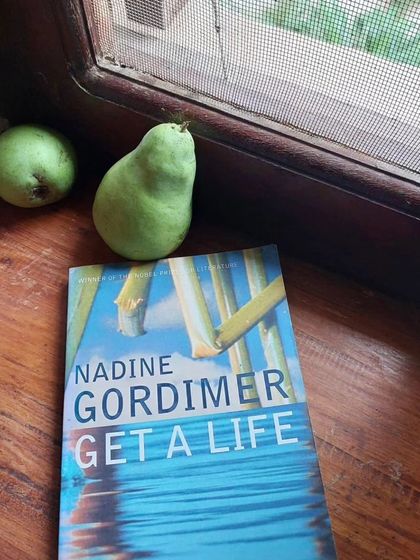 A book, "Get a Life" by Nadine Gordimer, resting on a windowsill with fresh pears. A quiet moment of reading and reflection at the retreat.