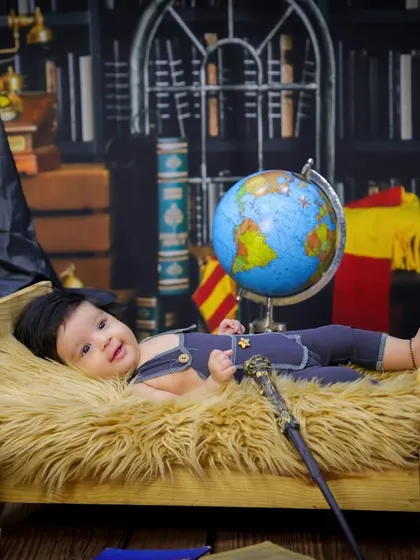 A wide shot of our Harry Potter theme, showing the baby on a miniature bed surrounded by books, globes, and a sorting hat for a complete magical library feel.